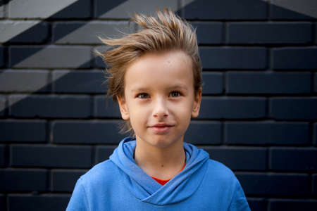 Funny portrait of a blonde caucasian boy whose hair rises and flies in the wind. Looks at the cameraの写真素材
