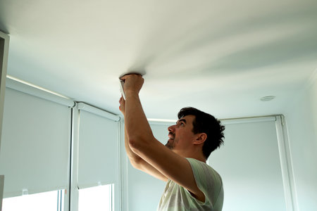 House master male electrician repairs ceiling light indoor home in white roomの写真素材