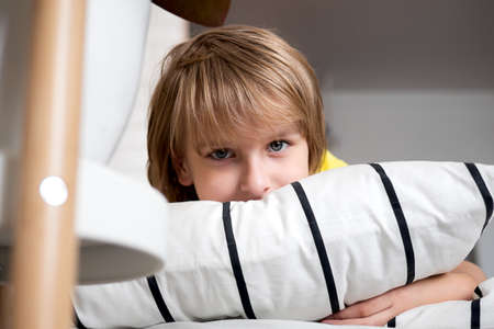 A blond boy in a yellow T-shirt lies on the bed Having fun at home Happy kids childhoodの写真素材