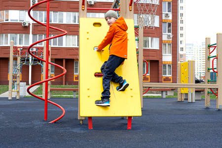 Funny caucasian blond boy in an orange jacket plays on the sports playgroundの写真素材