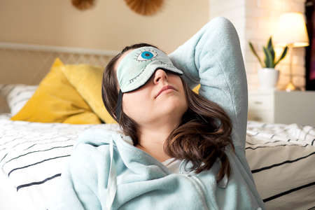 Middle aged woman in pajamas and sleep mask sitting relaxed on bed at homeの写真素材