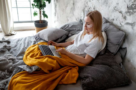 A beautiful young woman uses a laptop lying in bedの写真素材