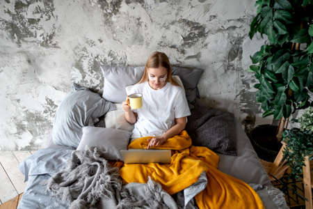 A beautiful young woman uses a laptop lying in bedの写真素材