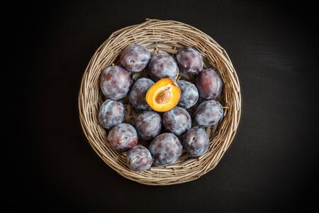 Fresh sweet plum in round rustic wicker basket on black chalkboard with copy space. One half of plum yellow  core.の写真素材