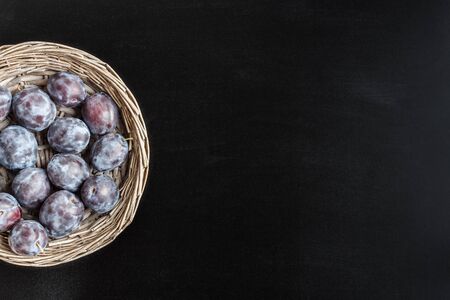 Fresh sweet plum in round rustic wicker basket on black chalkboard  with copy space.の写真素材