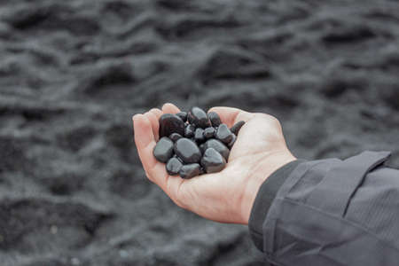 Hand holding small black rocks at Black Sand Beach, Icelandの写真素材