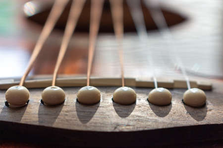 Acoustic guitar bridge with one pins and strings close up with selective shallow focus.の写真素材