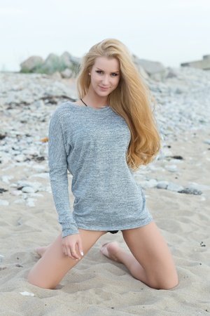 Beautiful young woman sitting on rock over sea at summerの写真素材