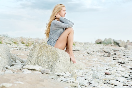 Beautiful young woman sitting on rock over sea at summerの写真素材