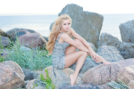 Beautiful young woman sitting on rock over sea at summerの写真素材