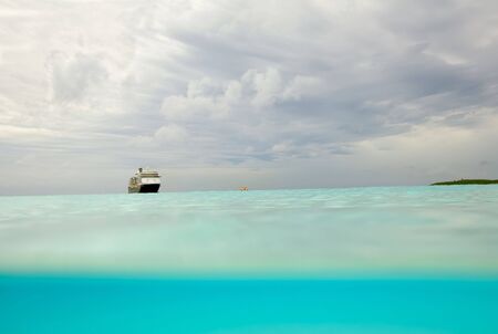 Dramatic sky viewed from partially under the waves of a beach in the Bahamas with an unidentifiable cruise ship in the backgroundの写真素材