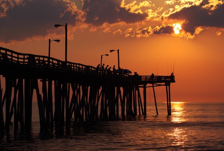 Early-morning anglers are silhouetted against the rising sun on a fishing pier in Nags Head, North Carolinaの写真素材