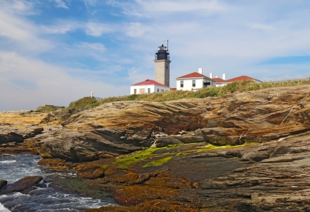 The Beavertail Light lighthouse near Jamestown on Conanicut Island, Rhode Island, viewed from the rocky coast with a bright blue sky and white cloudsの写真素材
