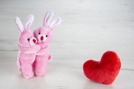 Pink toy bunnies hugging near red plush heartの写真素材
