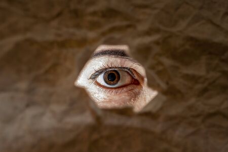 Brown eye of a girl with makeup looks into torn holeの写真素材