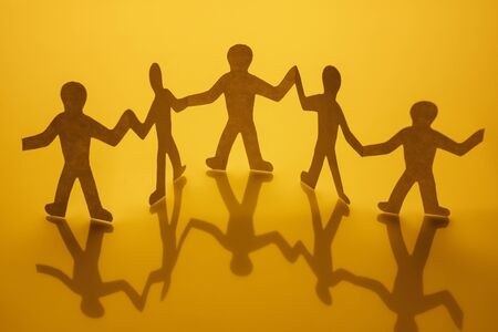 Concept of unity and humanity of people where paper men hold handsの写真素材