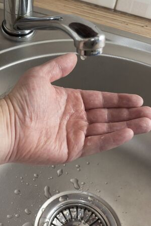 Drops of water drip in mans palm who checks if there is water in kitchen tapの写真素材