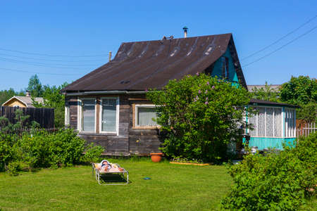 Girl on hot summer day sunbathes on a cottage lawn on cot in villageのeditorial素材