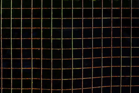 Square cells of rusty metal fence, with peeling paint, dark background pattern