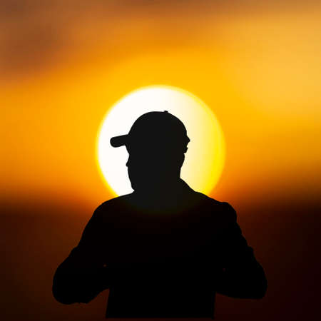 Silhouette of traveler in baseball cap on sunset sun backgroundの写真素材