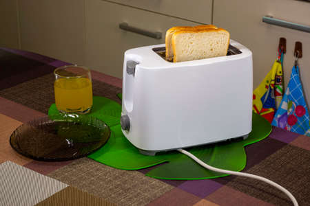 Toasts in toaster and glass of orange juice for breakfast on table