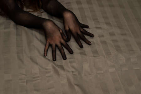 Graceful female hands in black seductive nylon glove on bedsheetの写真素材