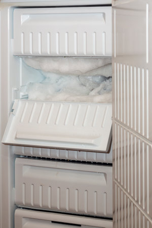 Large freezer is open, and one shelf is covered with iceの写真素材