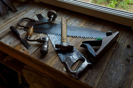 Vintage hacksaw, jointer, chisel, hammer and drill are on workbench in workshop