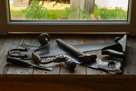 Vintage hacksaw, jointer, chisel, hammer and drill are in workshop by the window