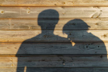 Shadow of man and woman on rustic wooden wall on sunny eveningの写真素材