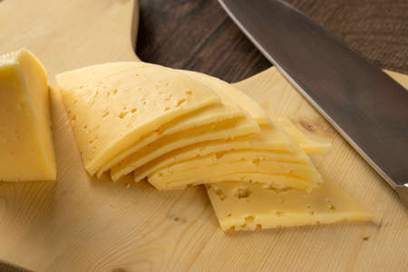 Thin slices of cheese on a wooden cutting boardの写真素材