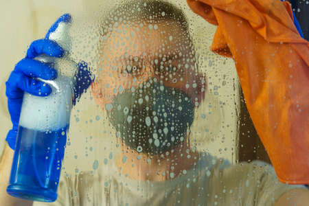 Man in respirator mask and gloves disinfects window surface with spray solution