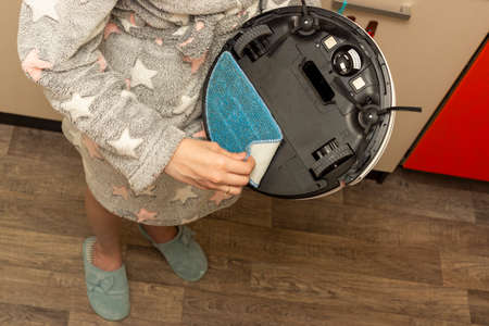 Woman in dressing gown removes rag of robot hoover after wet cleaningのeditorial素材