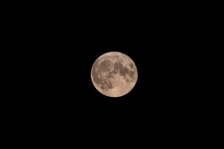 Closeup of the full moon with several craters visible on a dark background
