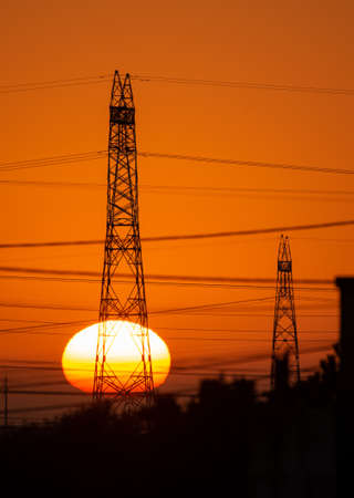 Electricity pylons and power lines in urban sunset, Silhouettes with big bright yellow sun on...