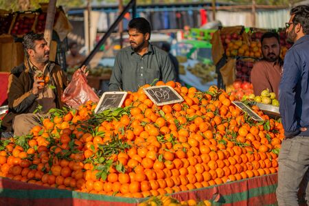 Islamabad, Islamabad Capital Territory, Pakistan - February 3, 2020, A seller is waiting for customers in the vegetable market to sell orange fruits.のeditorial素材