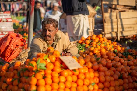 Islamabad, Islamabad Capital Territory, Pakistan - February 3, 2020, A seller is waiting for customers in the vegetable market to sell orange fruits.のeditorial素材
