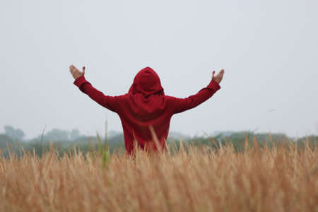 Woman in red hoodie with arms outstretched standing in wheat fieldの写真素材