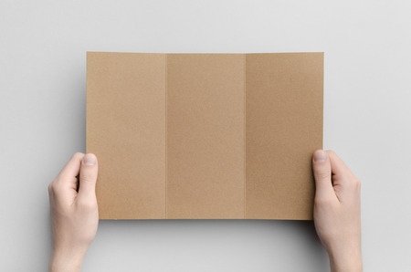 Kraft A4 Tri-Fold Brochure Mock-Up - Male hands holding a kraft tri-fold on a gray background.の写真素材