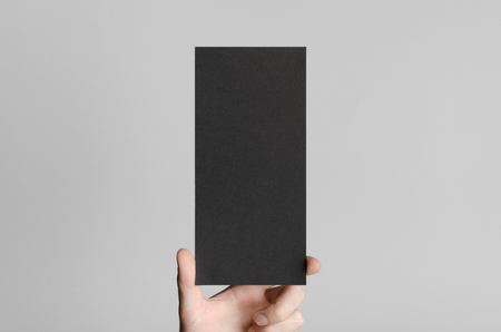 Black DL Flyer Mock-Up - Male hands holding a black flyer on a gray background.の写真素材