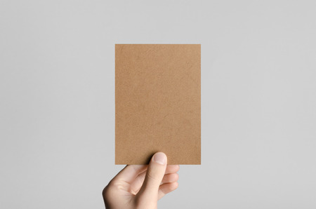 Kraft A6 Flyer / Postcard / Invitation Mock-Up - Male hands holding a kraft flyer on a gray background.の写真素材