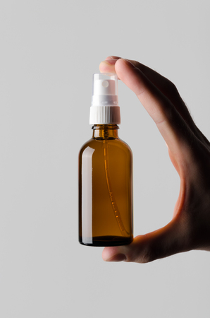 Amber Spray Bottle Mock-Up - Male hands holding an amber spray bottle on a gray backgroundの写真素材