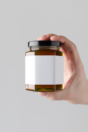 Honey Jar Mock-Up. Blank Label - Male hands holding a honey jar on a gray backgroundの写真素材