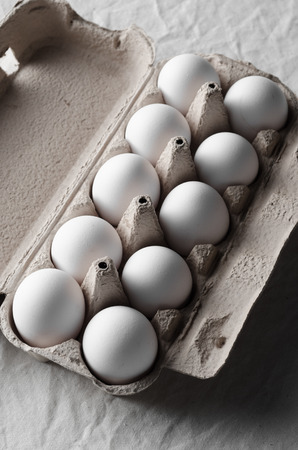 White eggs in an egg carton. White linen tablecloth background.の写真素材