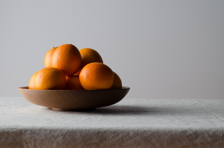 Oranges in a wooden bowl on a white linen tablecloth.の写真素材