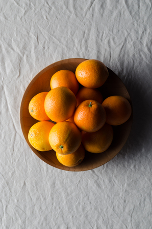 Oranges in a wooden bowl on a white linen tablecloth.の写真素材