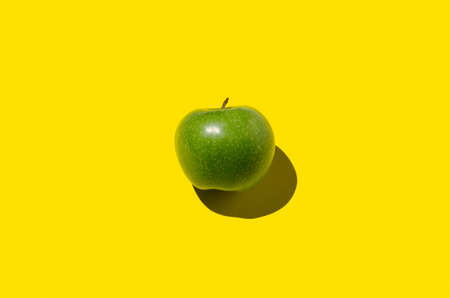 Green apple on a yellow background. Hard shadow, overhead.の写真素材