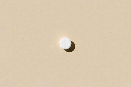 Round tablet pill on a beige background. Hard shadows.