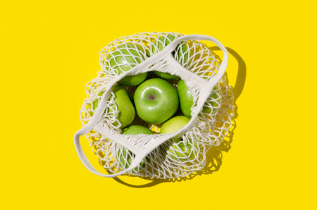 Green apples in a reusable mesh bag on a bright yellow background. Zero waste concept