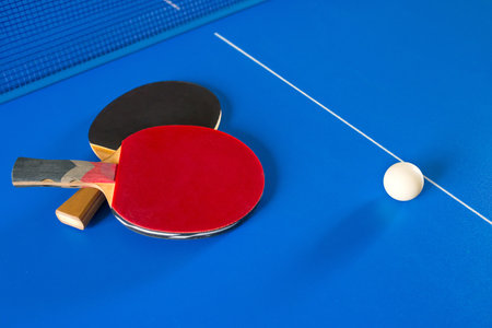Two rackets for table tennis and a white ball on the blue table. A game. Sport games.の写真素材